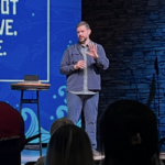Man speaking on church stage with blue backdrop